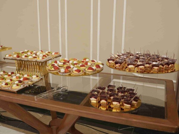 Dessert buffet with fruit tartlets and layered cake cups arranged on gold trays at an indoor event venue.