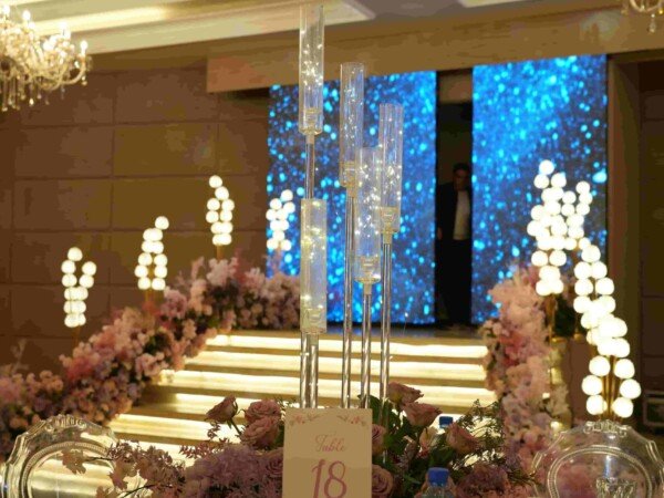 Wedding reception table with pink floral centerpiece and crystal candleholders facing a glowing blue stage backdrop.