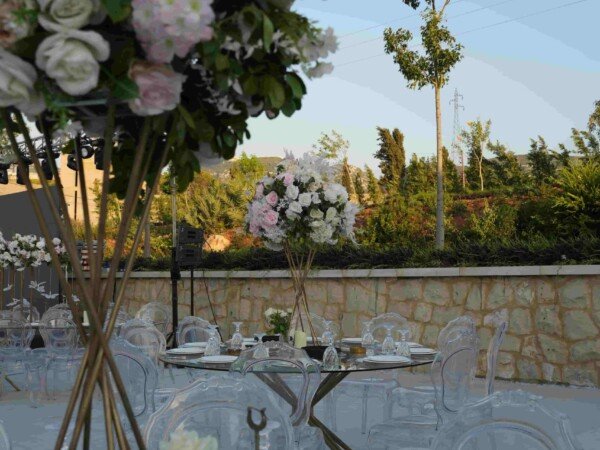 Outdoor wedding table setting with clear chairs, glass tables, floral centerpieces, and elegant place settings in a garden venue.